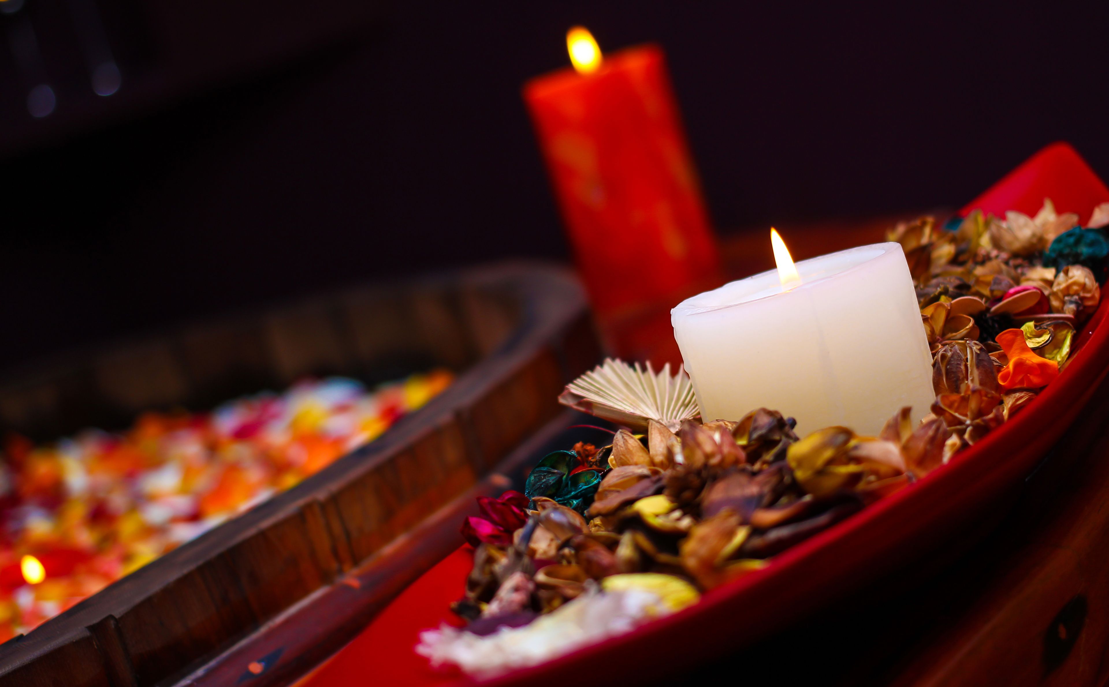 A candle in a red holder surrounded by dried flowers and shells.