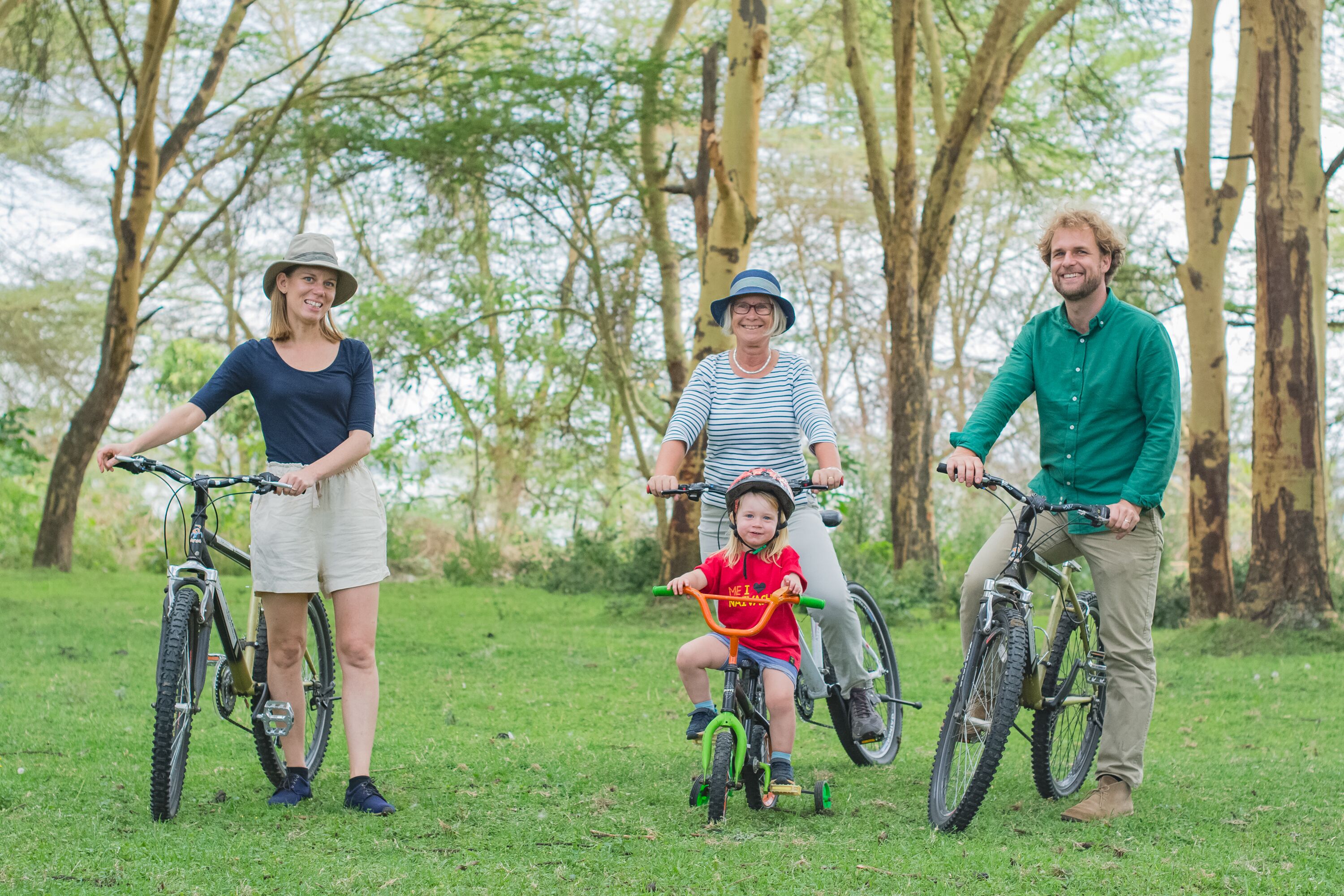 Una familia en bicicleta en un área con césped y árboles de fondo.