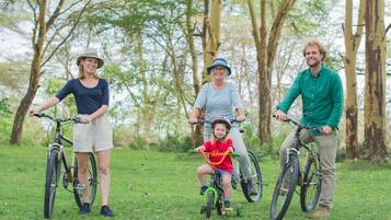 Una familia en bicicleta en un área con césped y árboles de fondo.