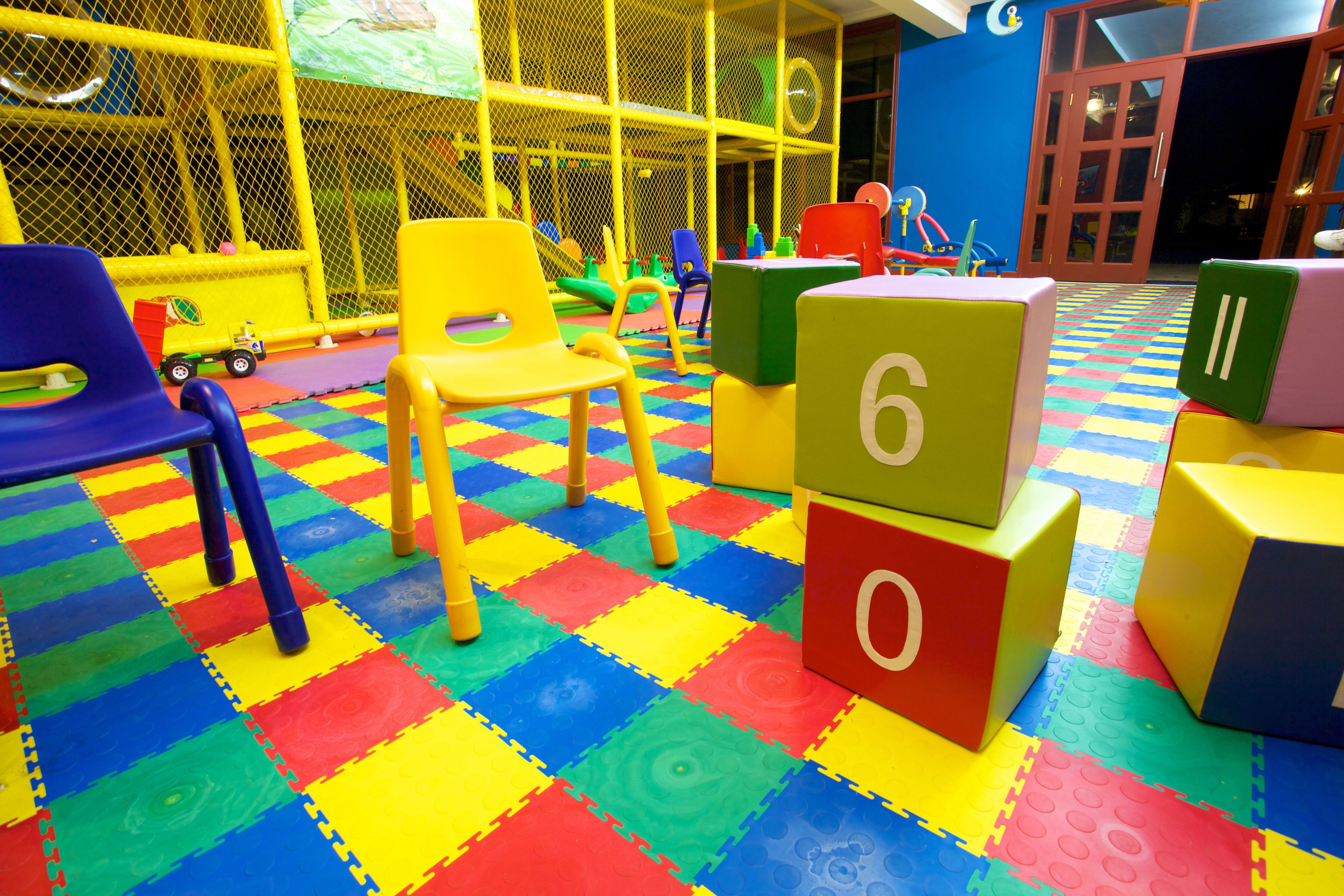 A play area with colorful interlocking foam mats, a yellow play structure, and a blue chair.