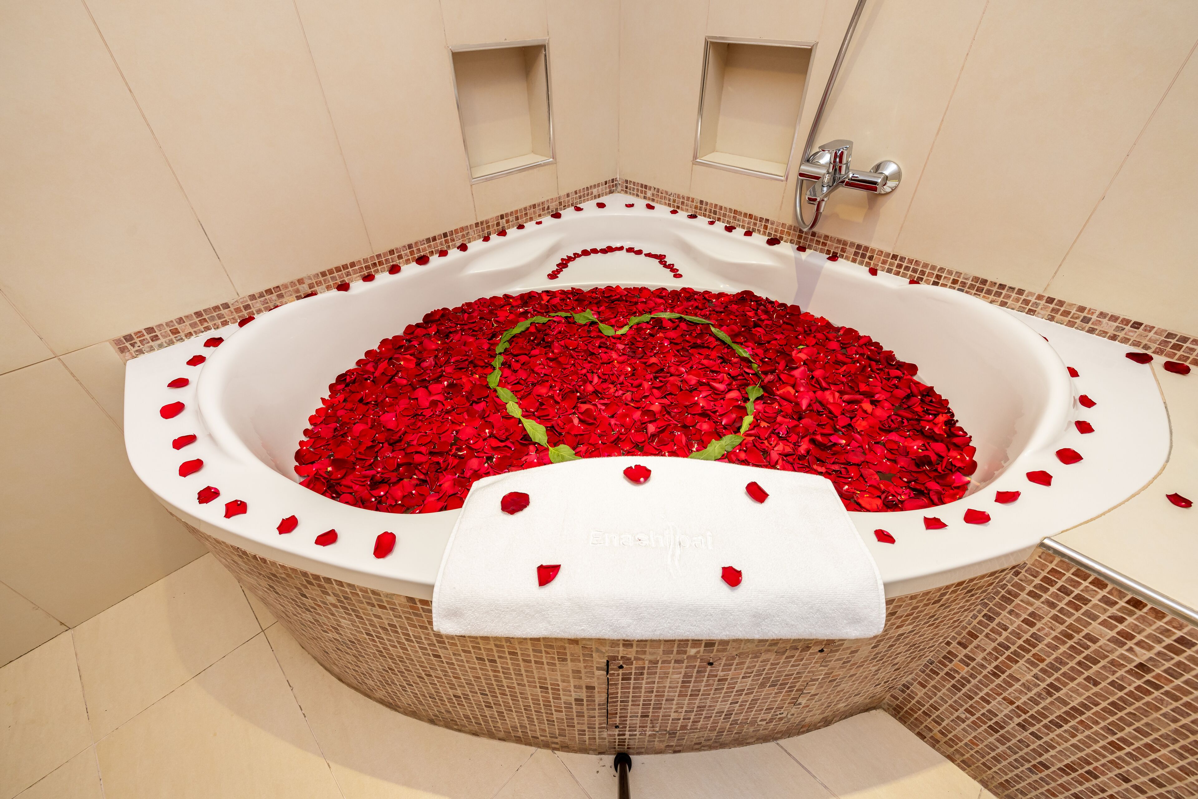 A bathtub filled with red rose petals arranged in a heart shape, with a white towel draped over the side.