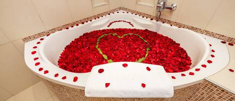A bathtub filled with red rose petals arranged in a heart shape, with a white towel draped over the side.