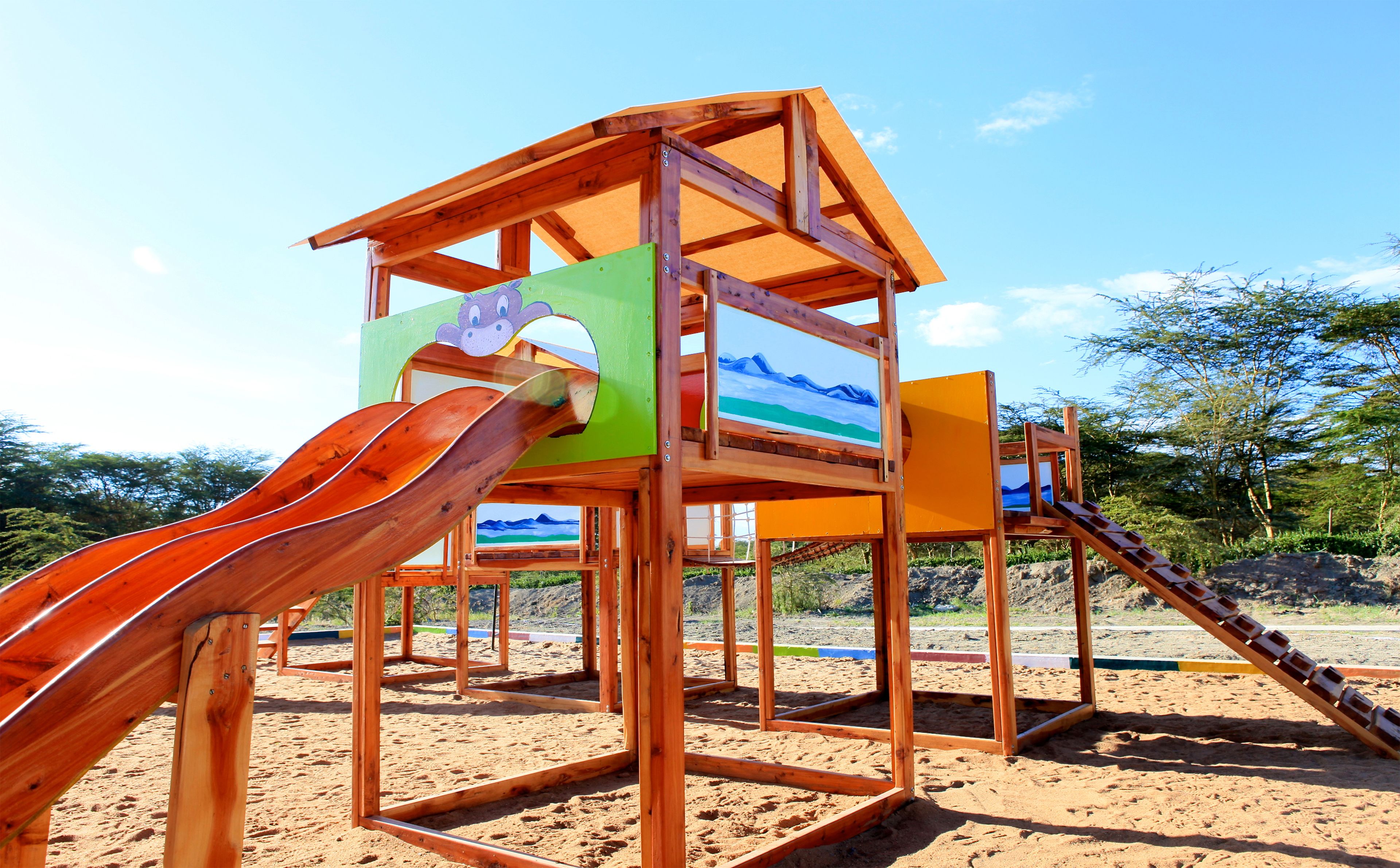 A wooden play structure with slides and climbing areas on a sandy beach.