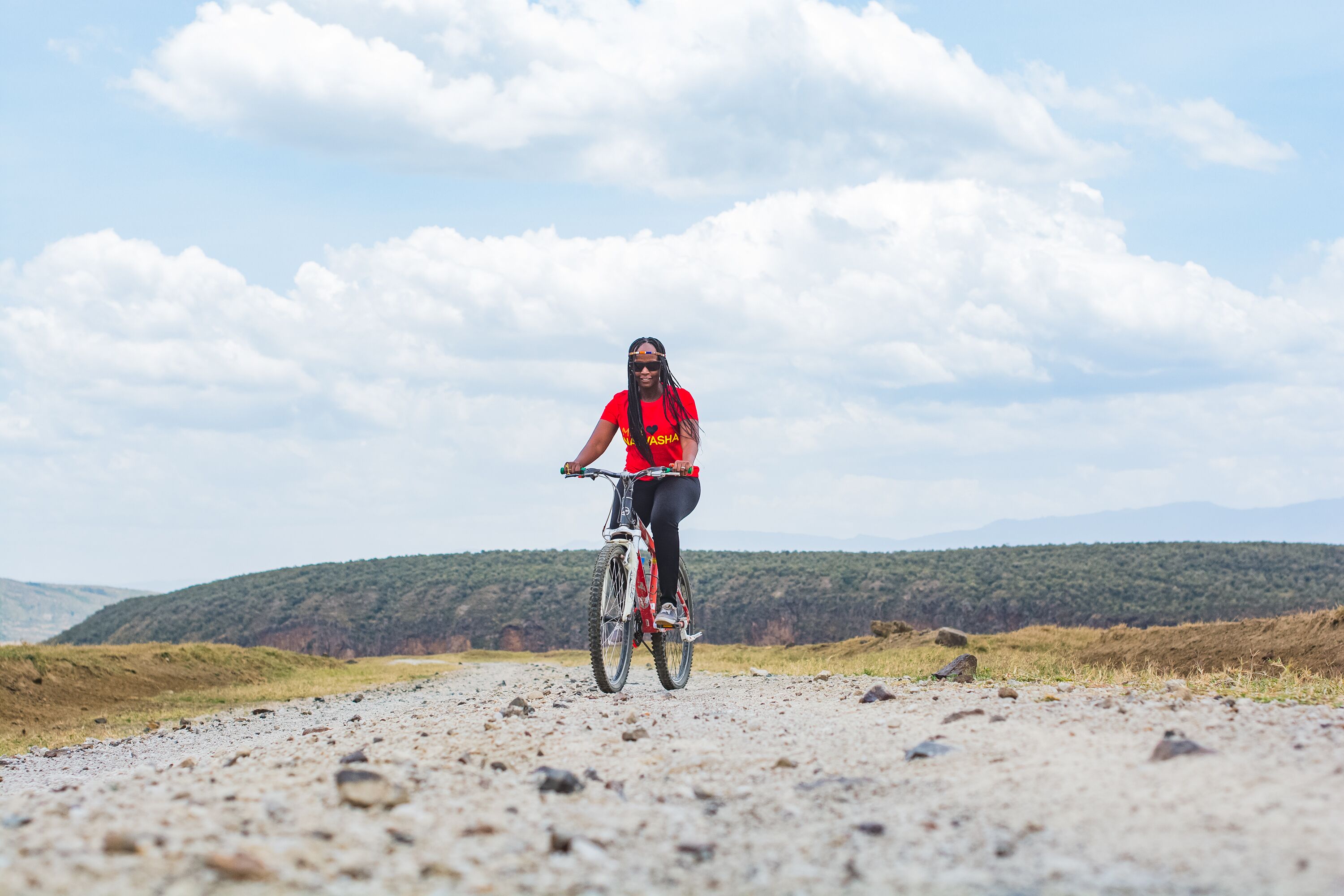 A person riding a bicycle on a gravel path with a mountainous landscape in the background.
