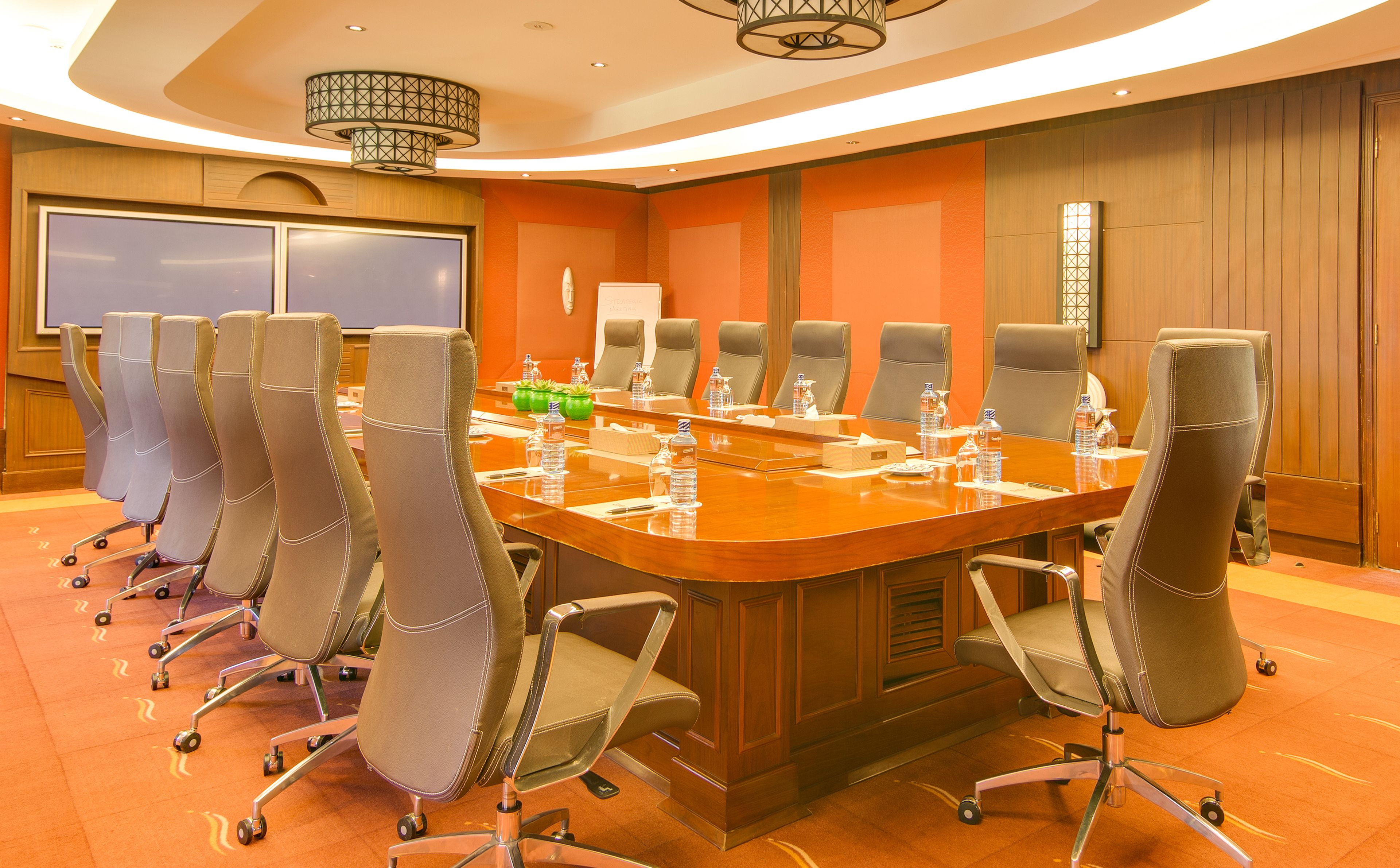 A conference room with a long table, multiple chairs, and a large screen.