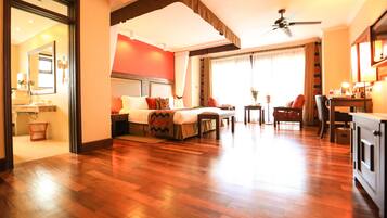 A hotel room with a bed, a desk, a chair, a small table, and a ceiling fan.