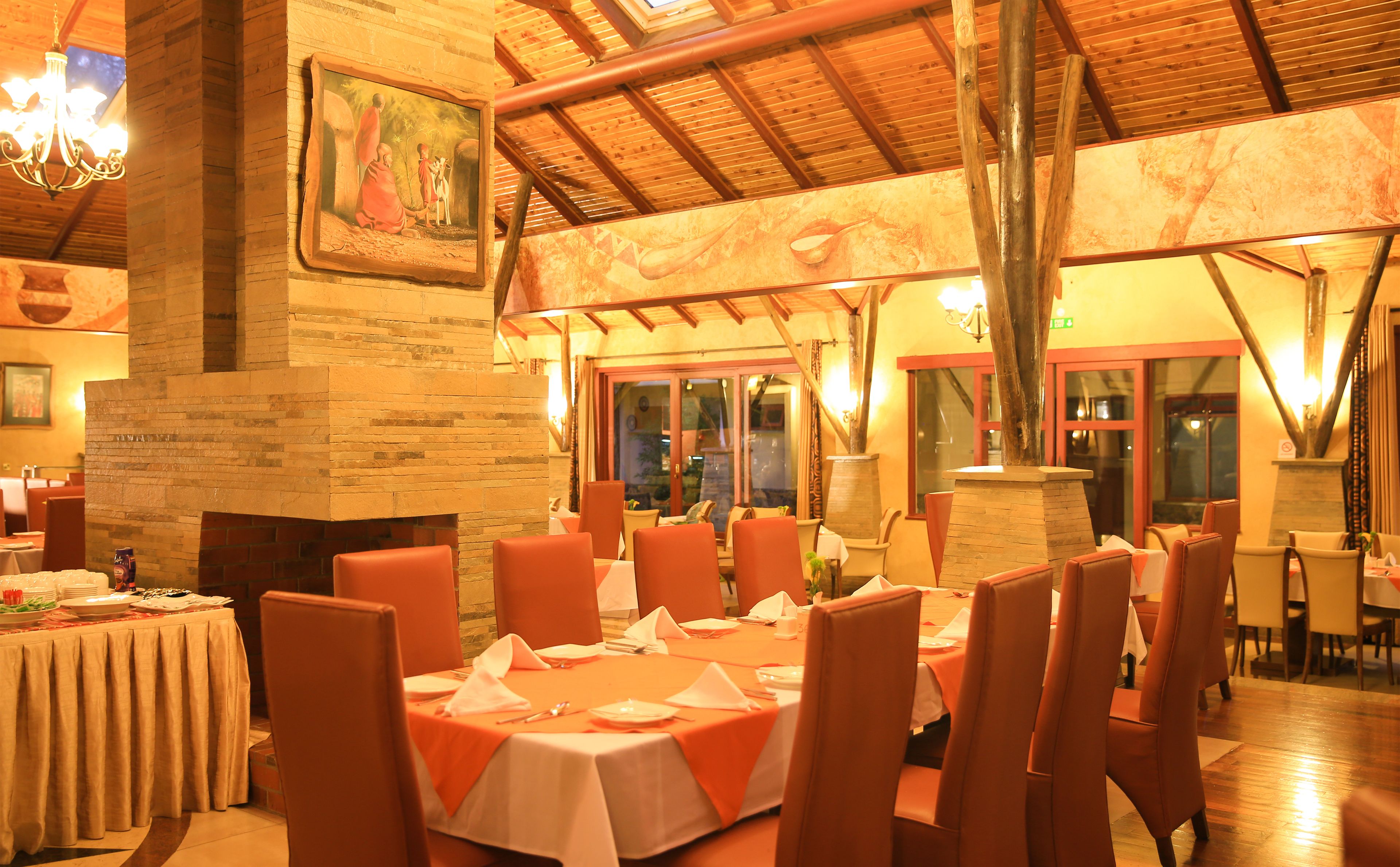 A restaurant with brick walls, wooden beams, and orange chairs. Tables are set with white tablecloths and napkins.