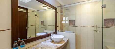 Un baño con un espejo grande, dos lavamanos, una cabina de ducha de vidrio y encimera de granito.