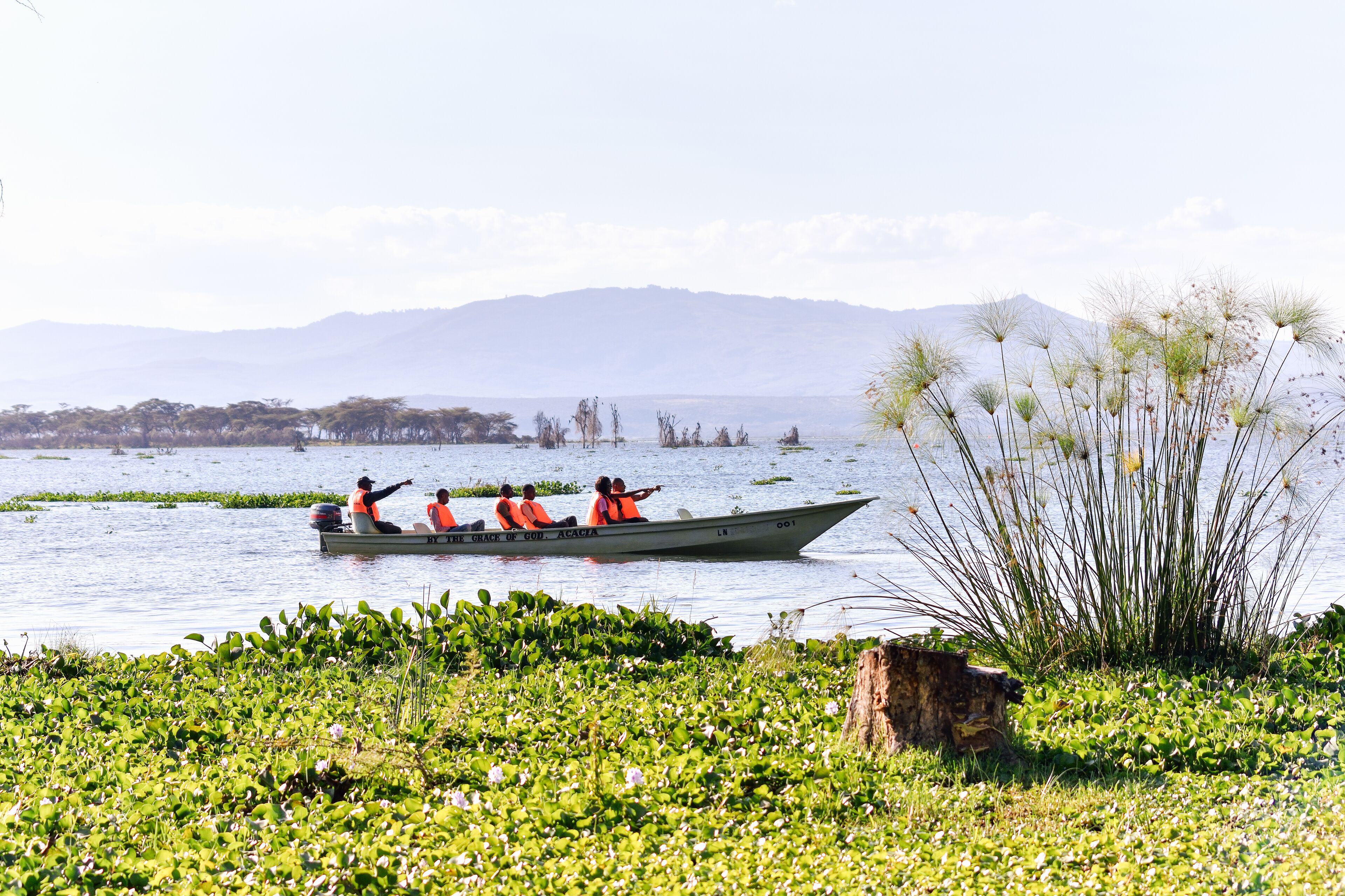 A boat with four people wearing orange life jackets on a calm body of water.