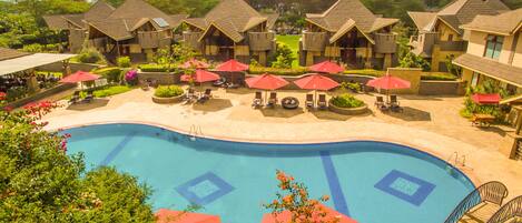 A resort with a swimming pool, red umbrellas, and multiple bungalow-style buildings.