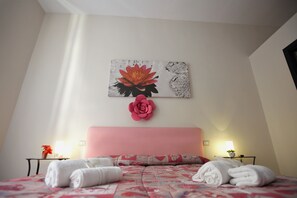 A hotel room with a pink headboard, a bed with floral bedding, two bedside tables with lamps, and a wall-mounted artwork of a flower. - Domus Armenio (Naples)