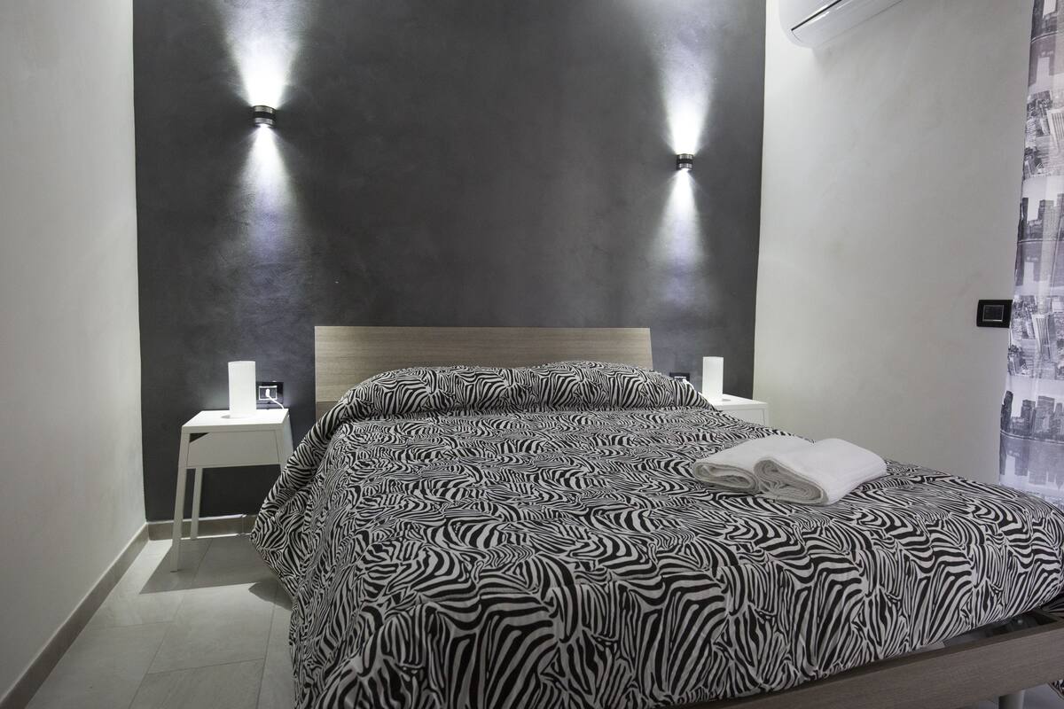 A hotel room with a zebra-patterned bedspread, a wooden headboard, two bedside lamps, and a small white nightstand.