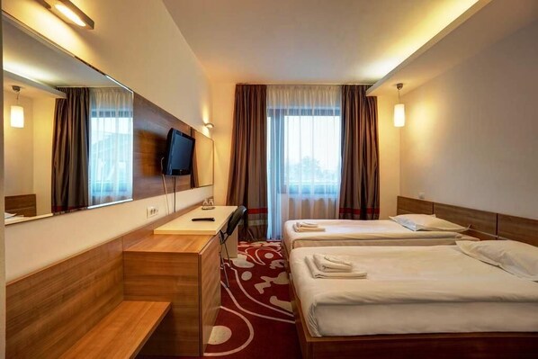 Una habitación de hotel con un escritorio de madera, dos camas, un televisor y un espejo grande.