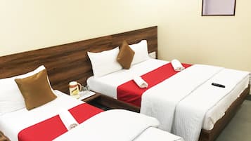 Two single beds with wooden headboards, white bedding, red and brown pillows, and a remote control on the right bed.