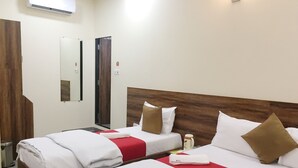 Ein Hotelzimmer mit zwei Betten, jeweils mit weißer Bettwäsche und roten Akzenten, einem Holzkopfende, einem Spiegel und einer wandmontierten Klimaanlage.