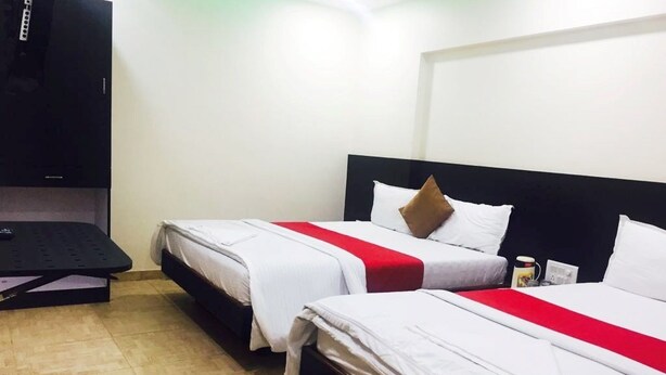 Ein Hotelzimmer mit zwei Betten, jeweils mit weißer Bettwäsche und roten Akzenten, einem schwarzen Kopfteil sowie einem an der Wand befestigten Flachbildfernseher.