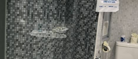 Un baño con zona de ducha, paredes de mosaico, inodoro blanco y una toalla de mano colgada en la pared.