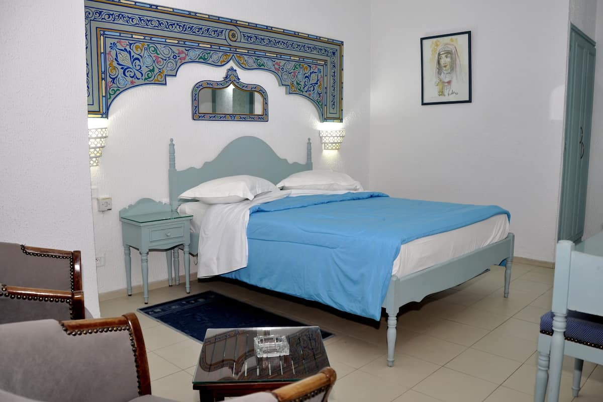 A bedroom with a bed, nightstands, a chair, a table, and a decorative wall piece.