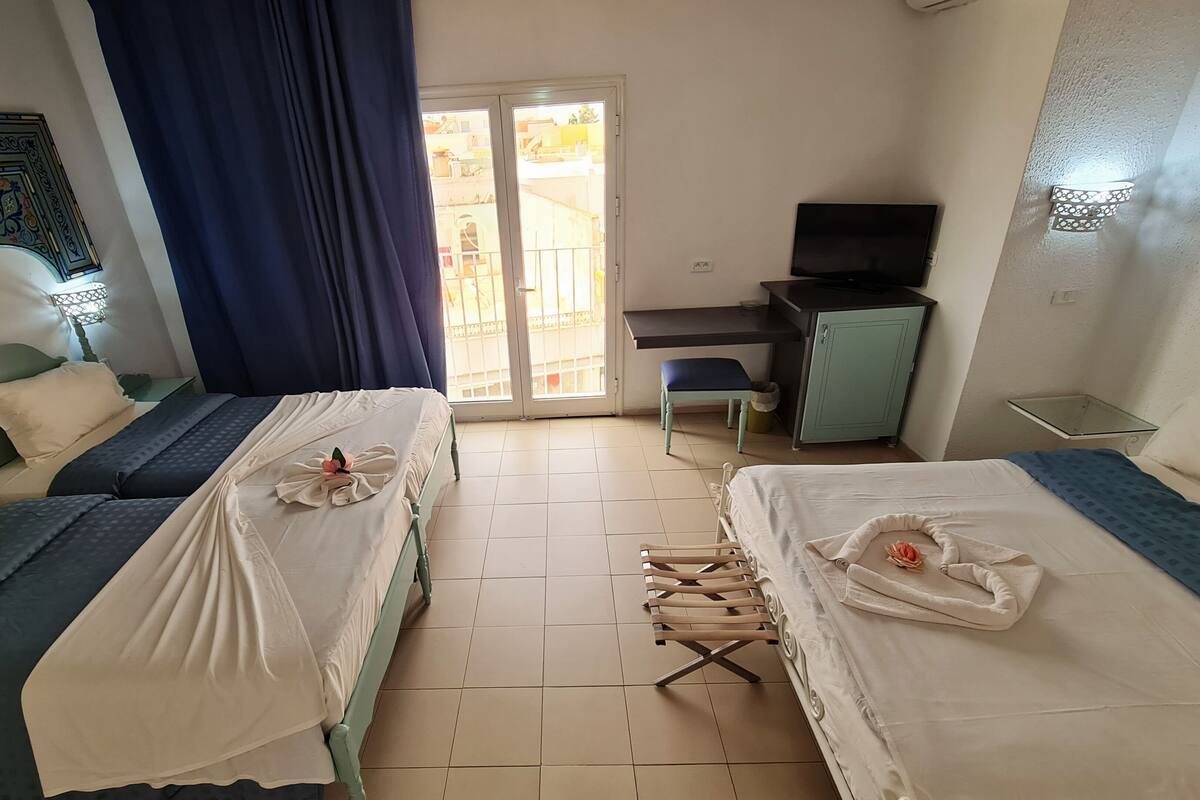 A hotel room with two beds, a desk, a TV, and a balcony.
