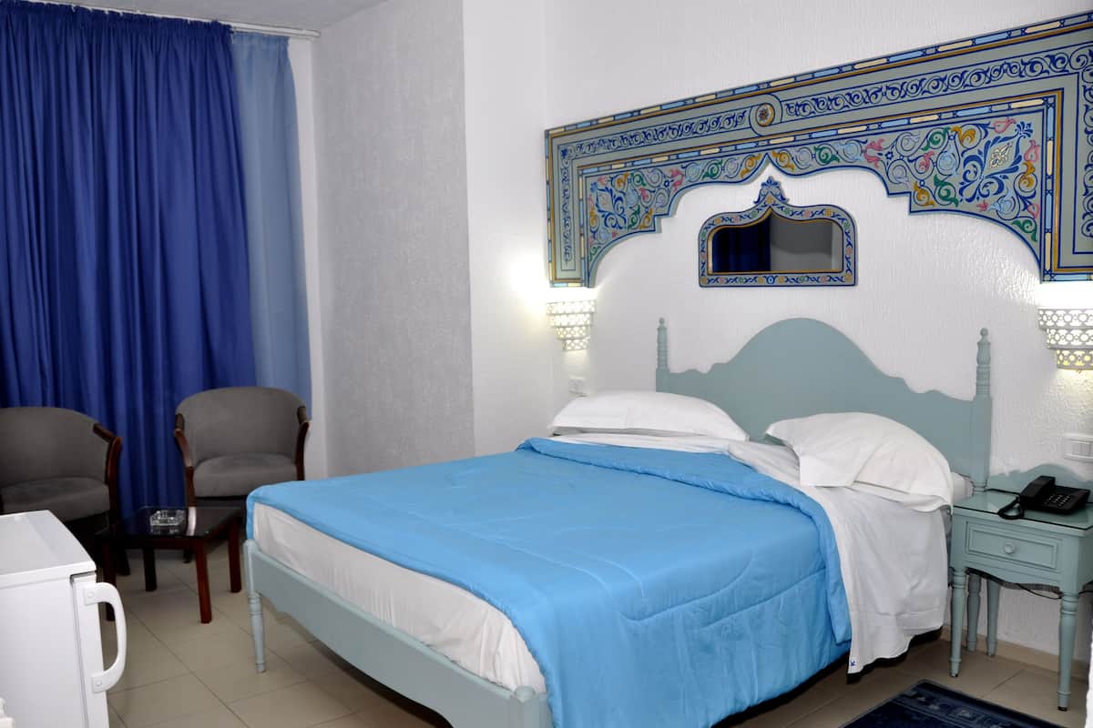 A hotel room with a bed, two chairs, a nightstand with a phone, and a decorative wall.