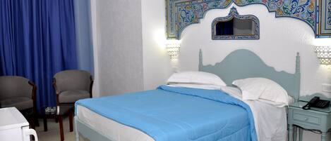 Quarto de hotel com cama, duas cadeiras, mesa de cabeceira com telefone e decoração na parede.