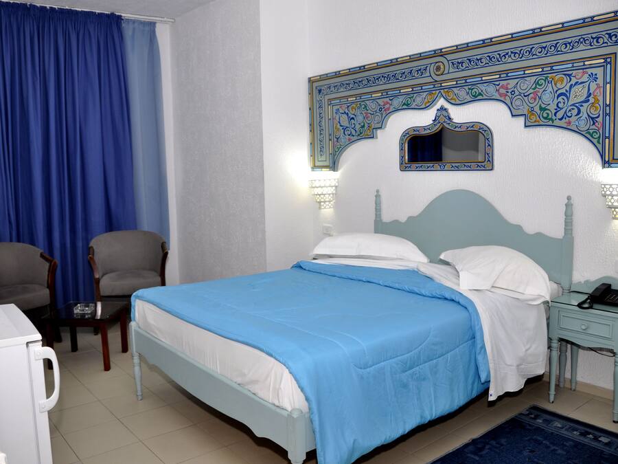 A hotel room with a bed, two chairs, a nightstand with a phone, and a decorative wall.