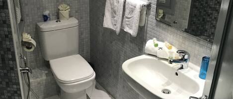 Ein Badezimmer mit Toilette, Waschbecken und Dusche. Auf dem Waschbecken liegen Handtücher und Toilettenartikel.