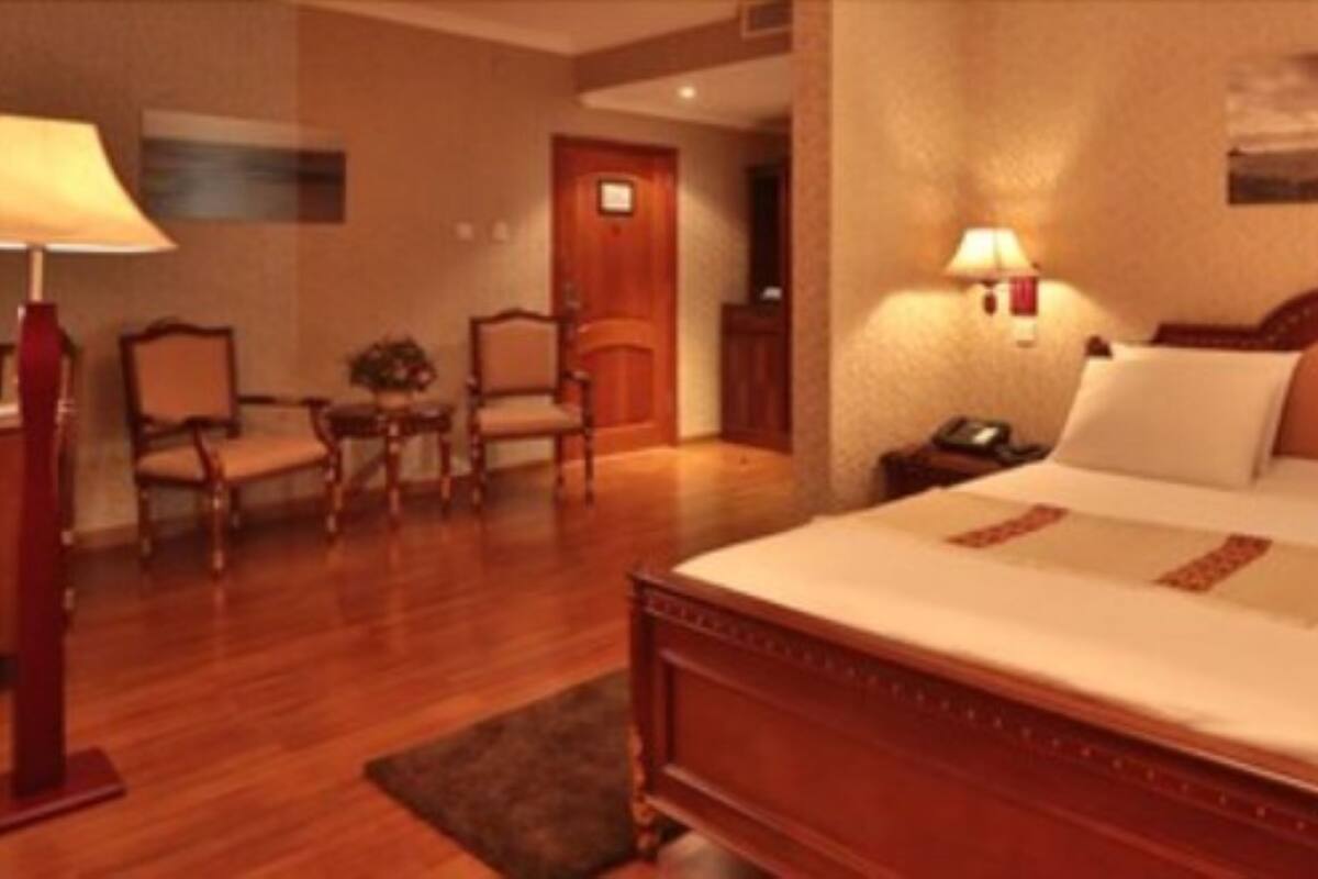 A hotel room with a large bed, two bedside lamps, a desk with a lamp, a chair, and a small table.