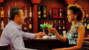 A bar setting with a man and a woman seated at a table, a bartender behind them, and a wall of liquor bottles. - Abyssinia Renaissance Hotel (Addis Ababa)