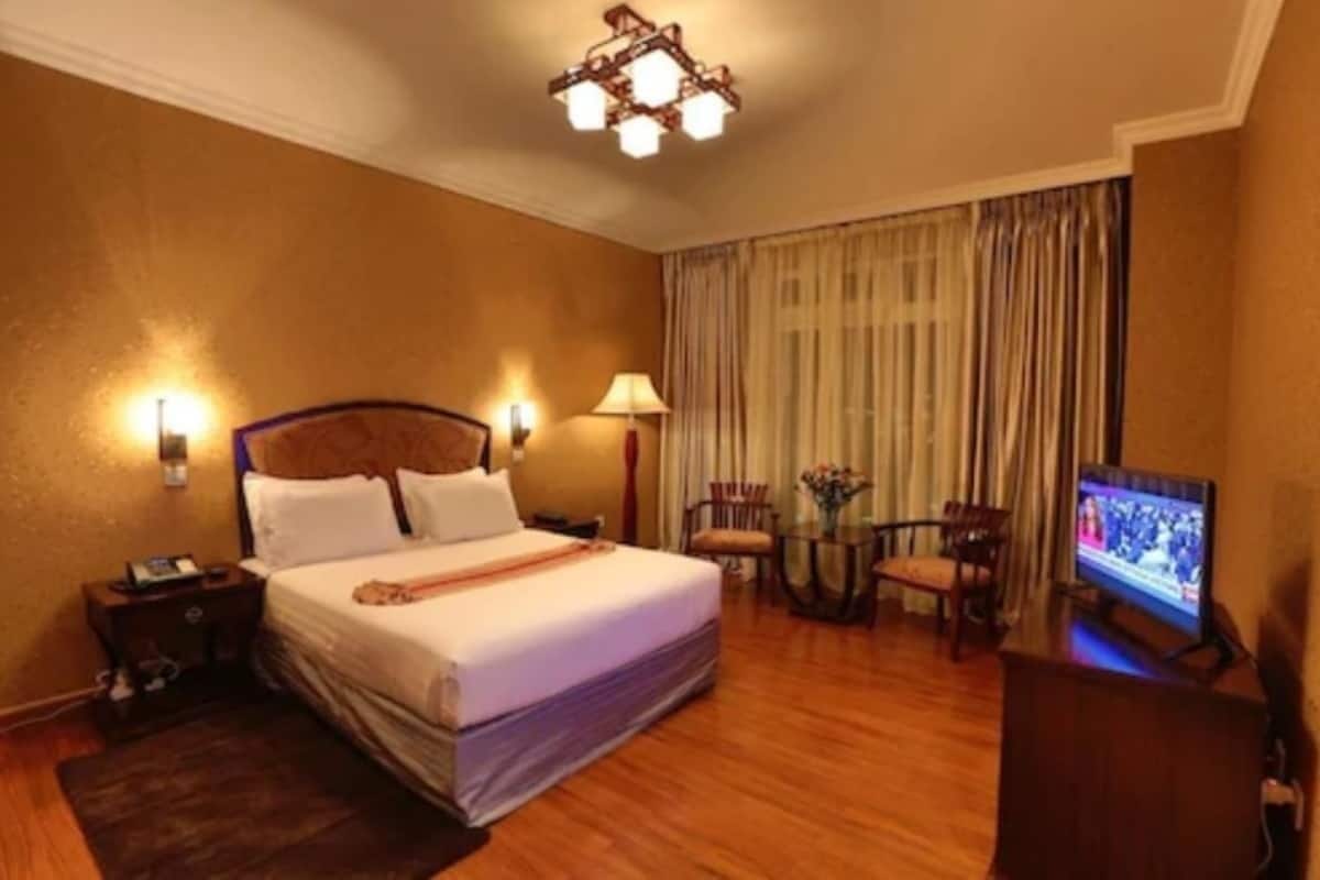 A hotel room with a large bed, bedside lamps, a television, and a small table with chairs.