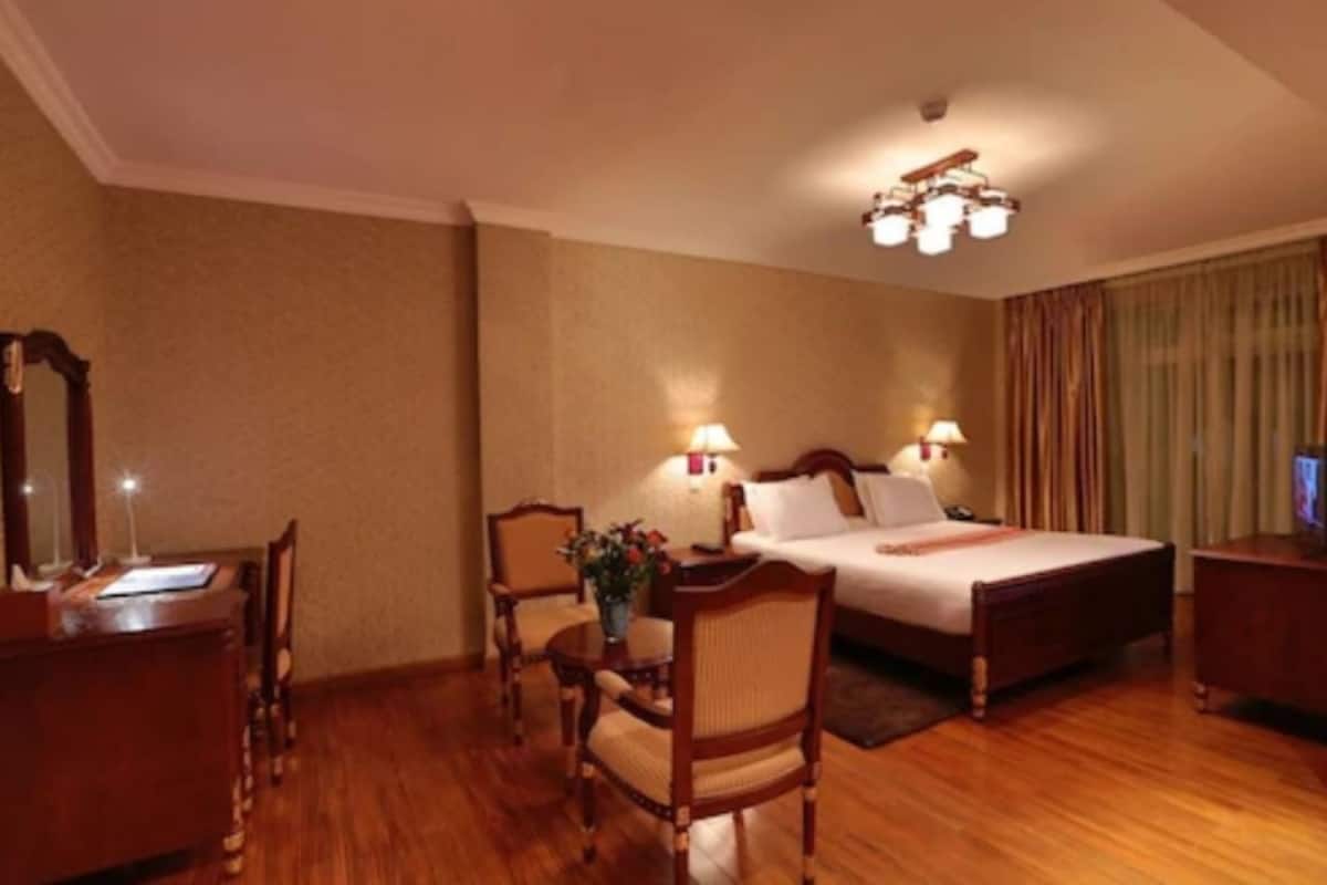 A hotel room with a bed, two bedside tables, a desk, a chair, and a lamp.