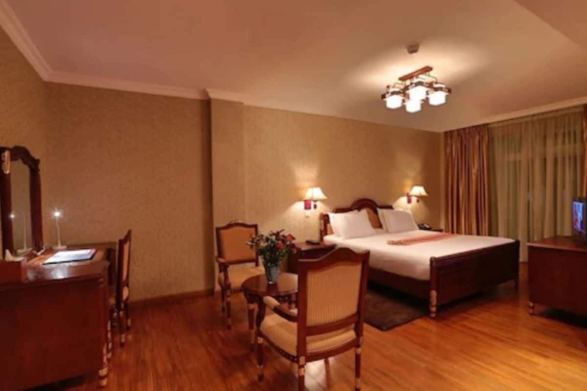 A hotel room with a bed, two bedside tables, a desk, a chair, and a lamp.