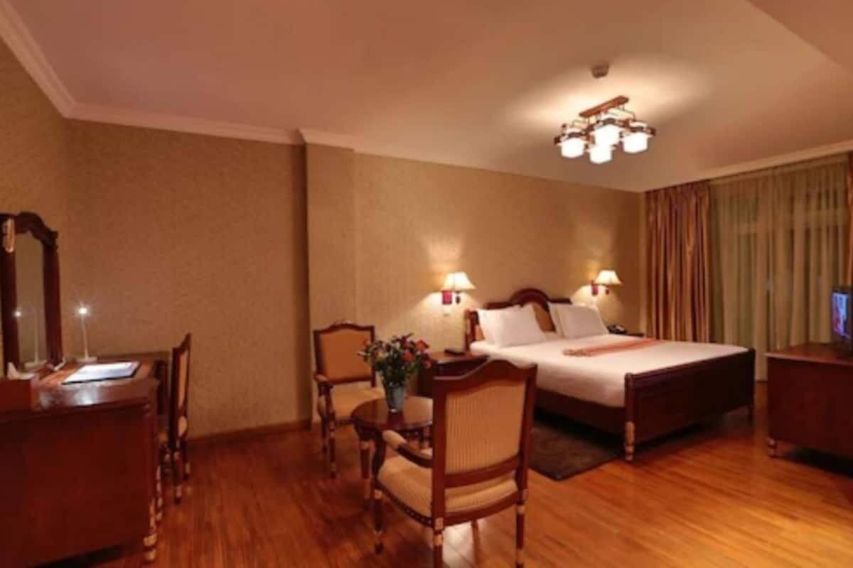 A hotel room with a bed, two bedside tables, a desk, a chair, and a lamp.