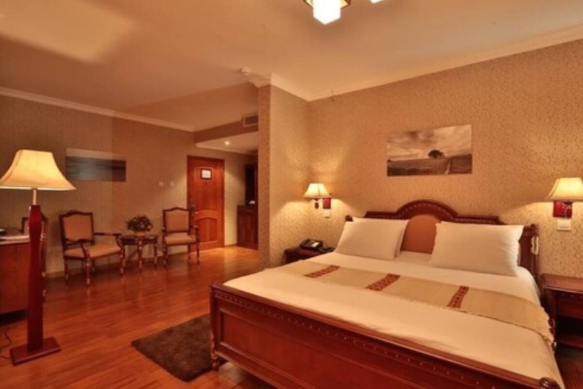 A hotel room with a large bed, two bedside tables, a desk with a lamp, and a chair.