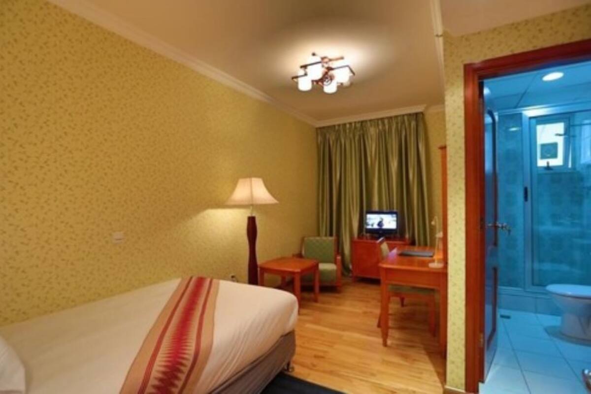 A hotel room with a bed, a desk, a chair, a television, and a bathroom visible through an open door.