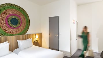 Habitación de hotel con dos camas, una obra de arte en la pared, una puerta y una silla.