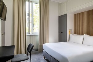 A hotel room with a bed, a desk, a chair, and a window with curtains.