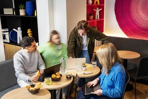 Et moderne fællesarbejdsområde med runde borde, bærbare computere og snacks.