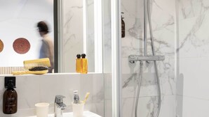 Un baño moderno con un lavamanos de mármol, cabezal de ducha de mano y un espejo que refleja a una persona.