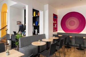 A modern interior with a grey sofa, round tables, black chairs, and a large abstract wall art piece.