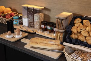 A breakfast buffet with bread, pastries, fruits, and condiments.