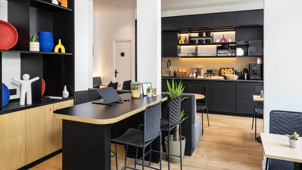 Una cocina moderna con gabinetes negros, encimera de madera y horno empotrado. Hay un comedor con una mesa y sillas negras.