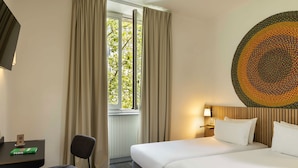 Habitación de hotel con cama, escritorio, silla, ventana con cortinas y pared con diseño circular.