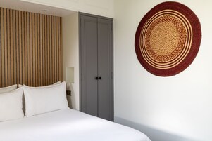 A bedroom with a bed, a grey wardrobe, a wooden slat headboard, and a circular woven wall hanging.