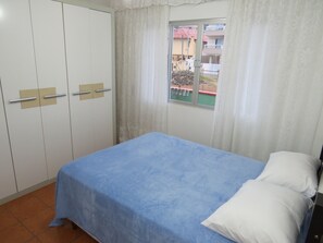 Quarto com uma cama de solteiro, janela com cortinas e um guarda-roupa.
