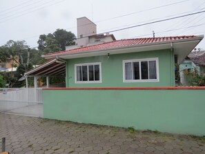 Uma casa térrea com fachada verde e telhado de telhas vermelhas.