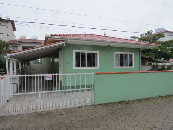 Uma casa residencial com fachada verde, telhado telhado e cerca branca.