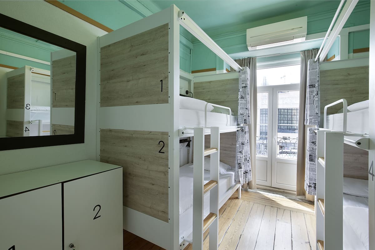 A dormitory room with bunk beds, a wardrobe, and a window with a view of the city.