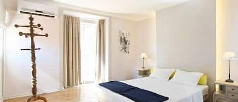 A hotel room with a large bed, a wooden floor, a coat rack, and a door leading to a balcony.