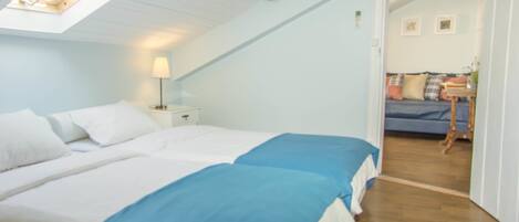 Un dormitorio con dos camas, un tragaluz, una mesita de noche con lámpara y vistas a otra habitación con sofá y una mesa.